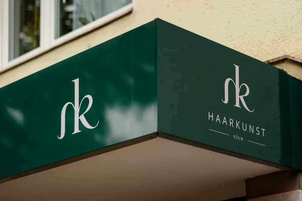 Grüne Markise mit eleganter Logo-Beschriftung im Eckbereich eines Geschäfts, umgesetzt von Werbetechnik Kleiner GmbH